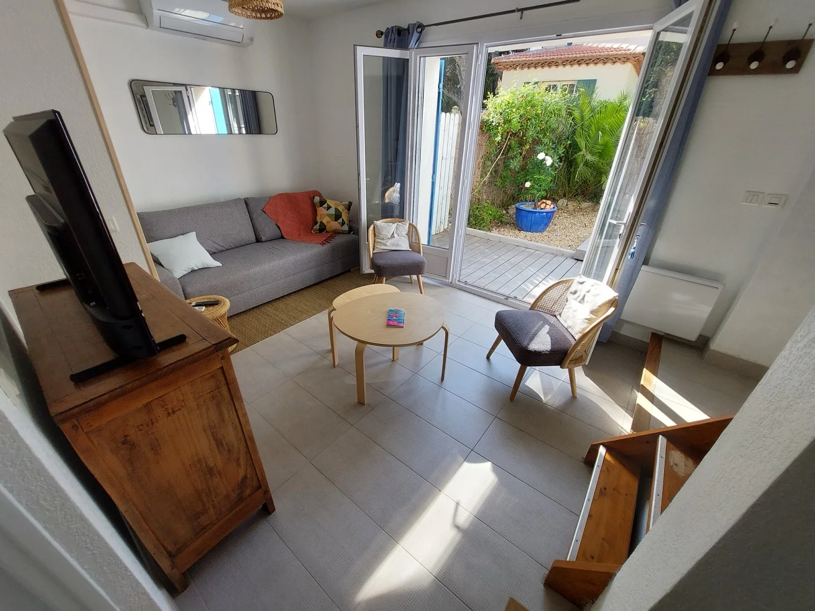 Salon ouvert sur le jardin avec canapé, fauteuils et TV